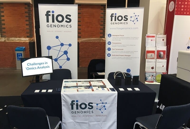 A standard Fios stand at a conference. There are two pull-up banners, a screen on a table with leaflets on the services offered.