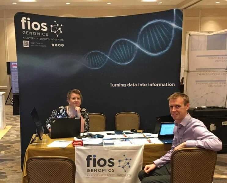 The Fios Genomics set up at the Biomarkers Congress in San Diego. The new dark blue Fios banner is behind a table, which Dr Sarah Lynagh and Dr Max Bylesjo are sitting at.